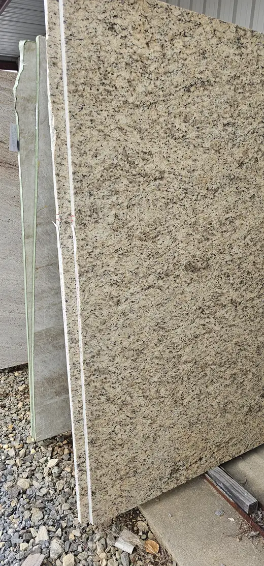 A full gold and black speckled granite slab standing on edge in the Byron stone yard, with paler quartzite slabs behind it